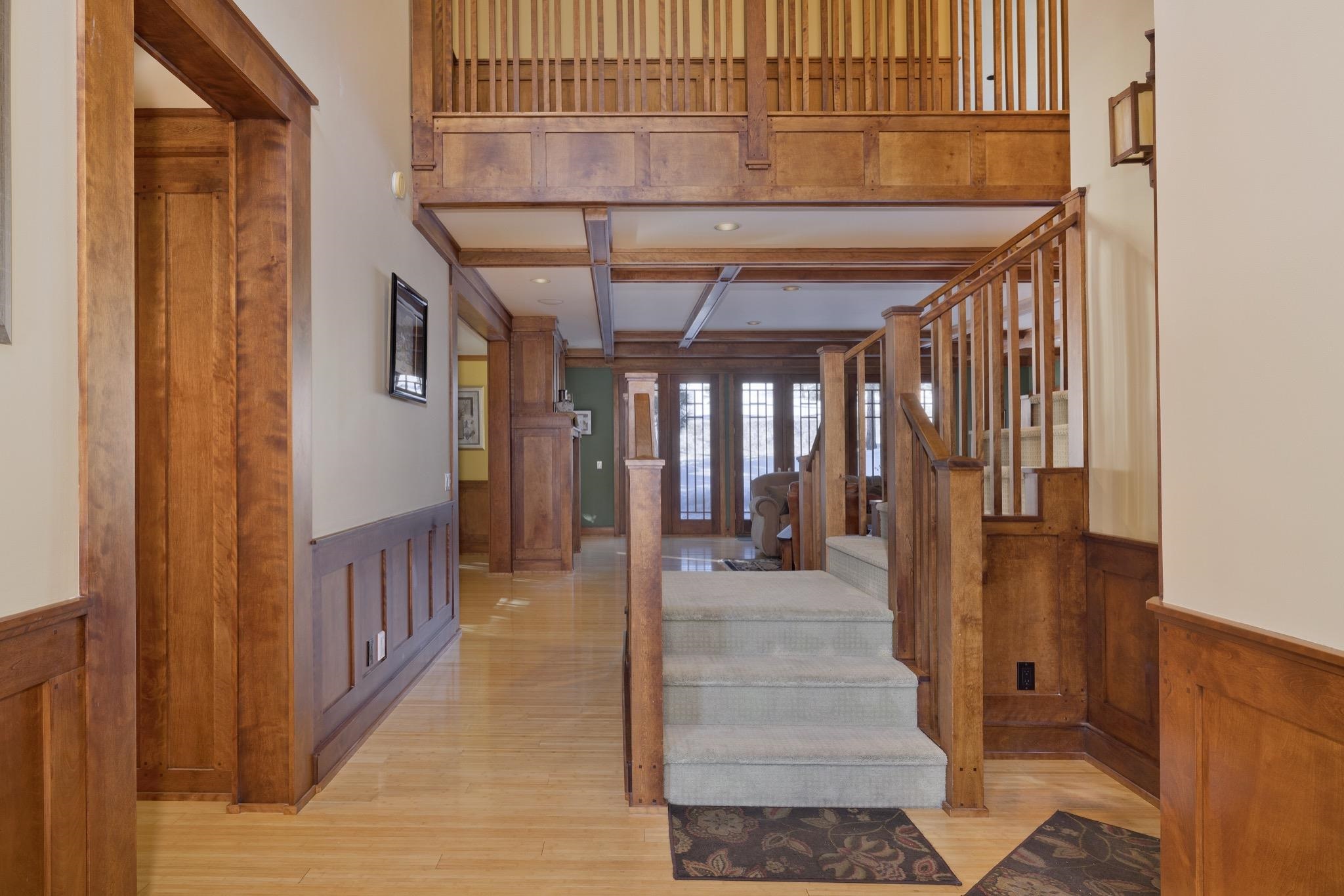 Wood-paneled entry hall with hardwood floors, carpeted stairs, and an upper-level landing.