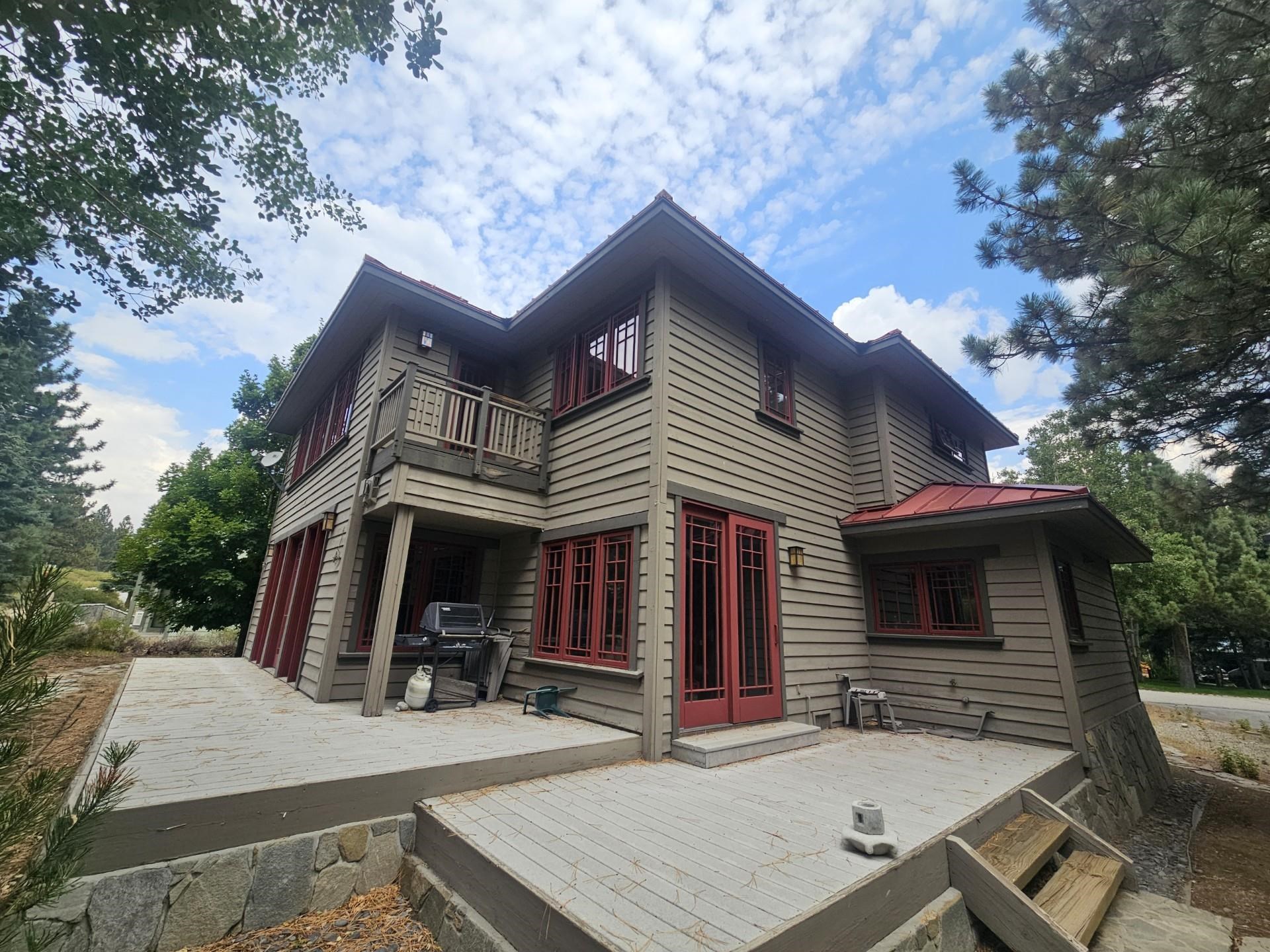 Two-story gray-sided home with red-trimmed windows and broad wooden decks among trees.