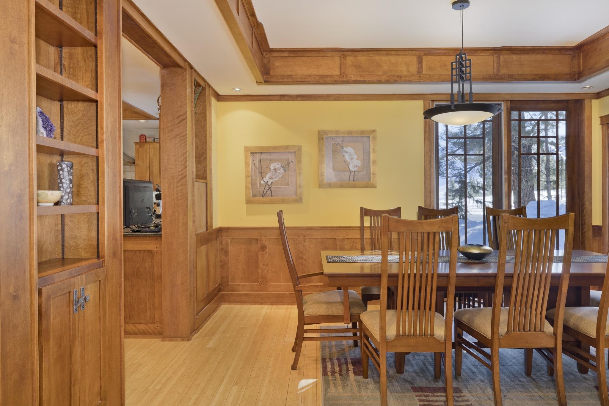 Dining room with wood paneling, built-in shelves, and snowy trees visible through large windows.