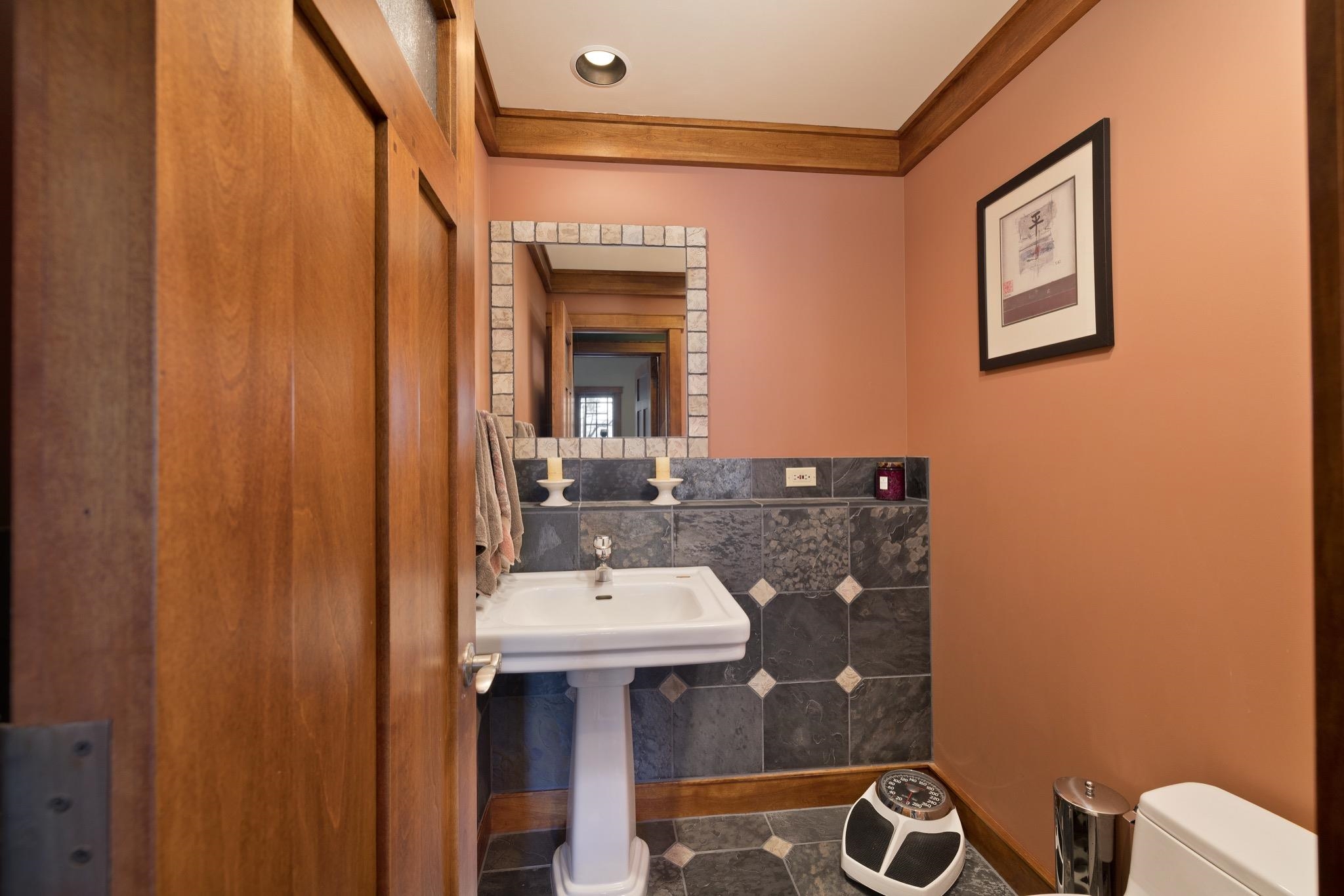 Bathroom with a white pedestal sink, framed mirror, and dark patterned tile.