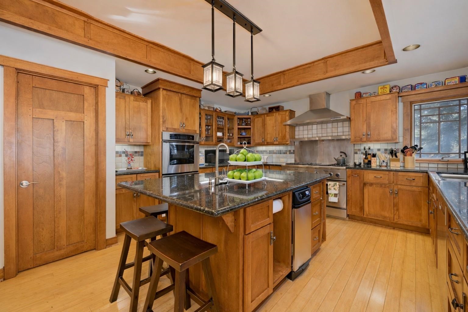 Kitchen with wood cabinetry, granite island, stainless appliances, and exposed ceiling beams.