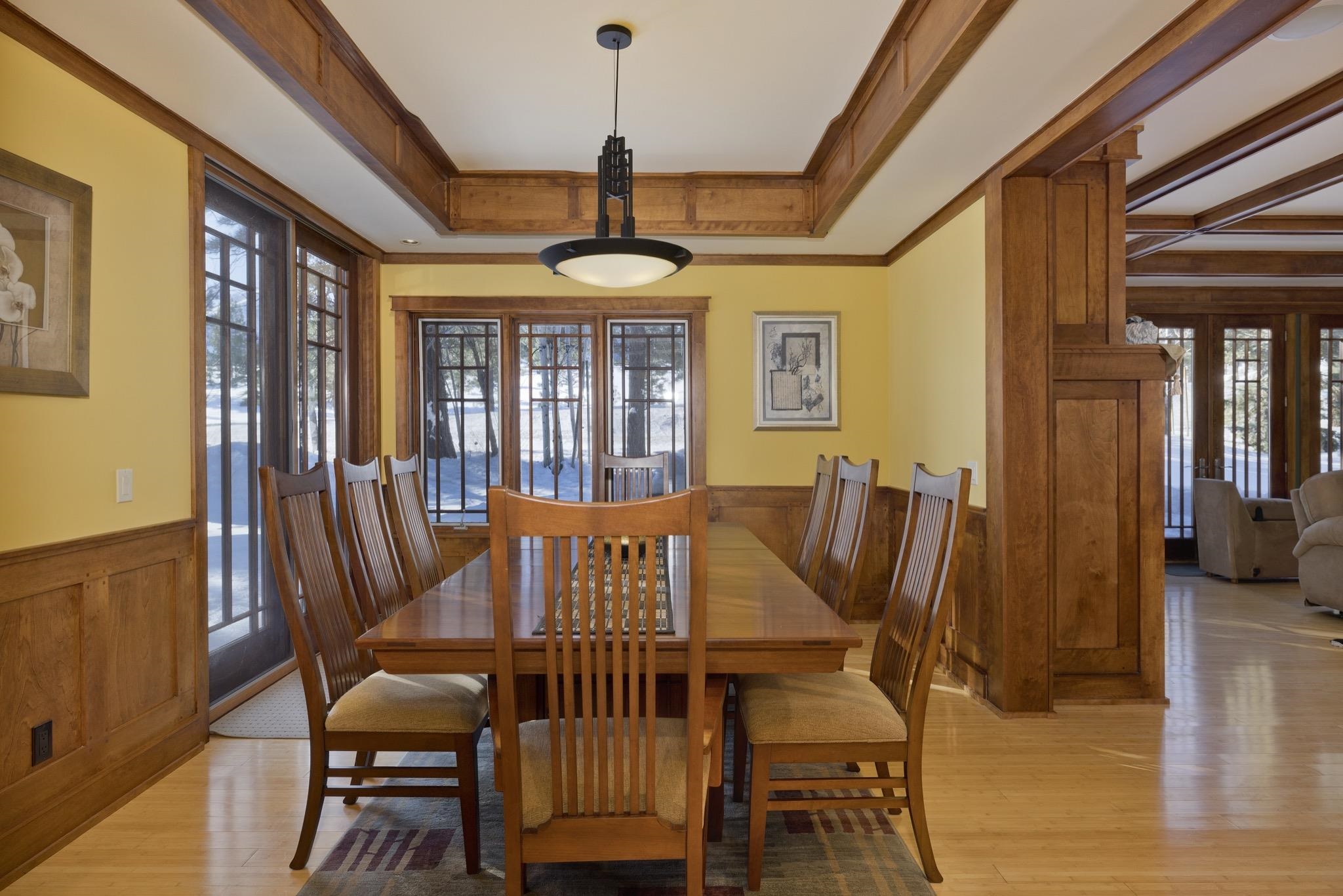 Dining room with a long wooden table, exposed beams, and windows overlooking snow.