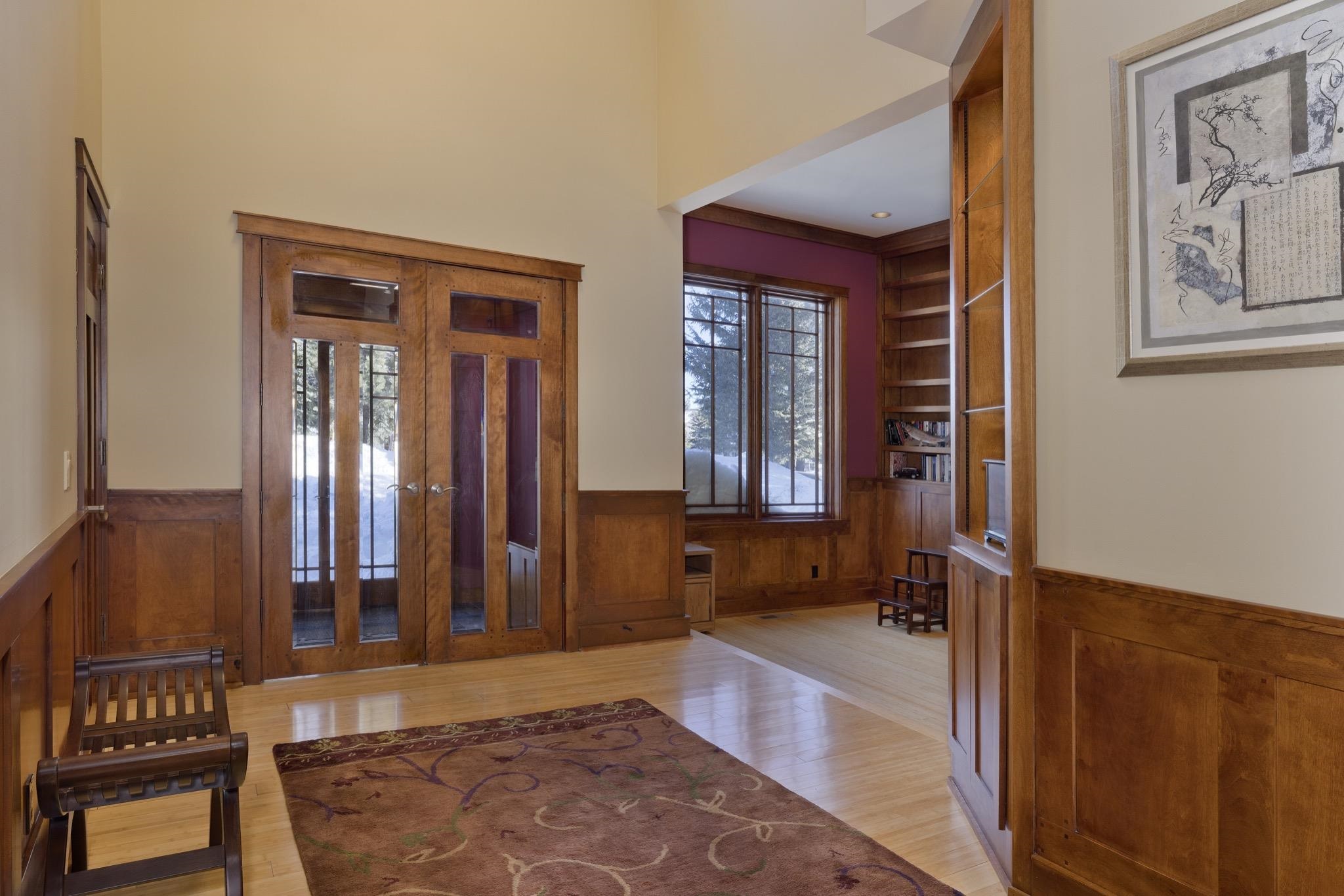 Wood-paneled entry hall with glass-paneled doors, built-in shelving, and snowy views through the windows.
