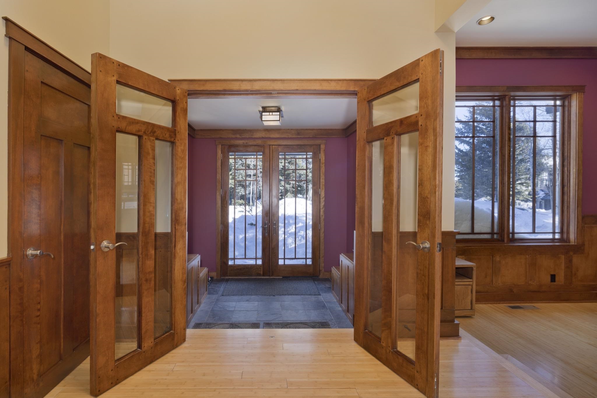 Entry hall with open glass-paneled wood doors and a snowy view through the foyer doors.