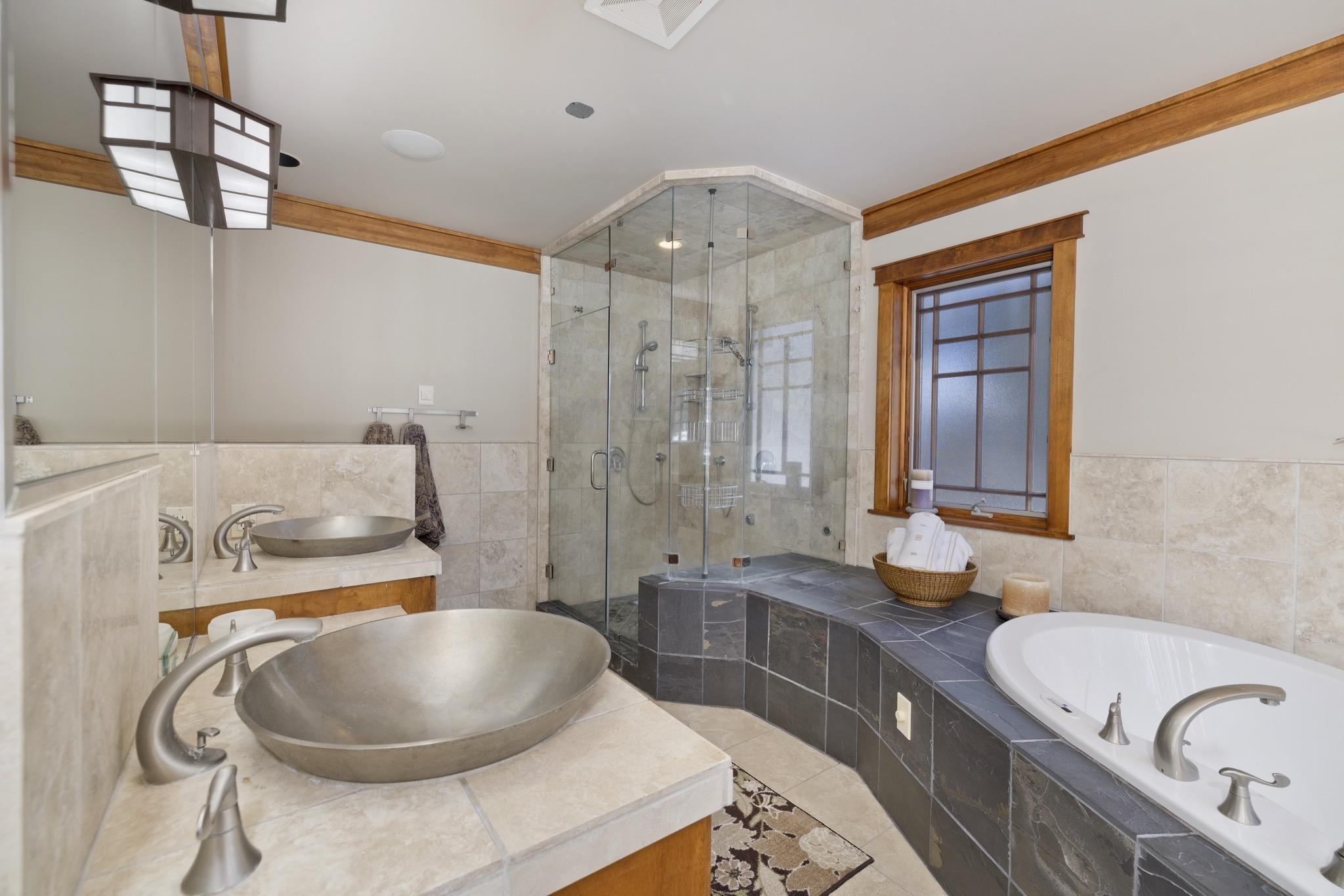 Bathroom with a glass shower, built-in soaking tub, and double vessel sinks.