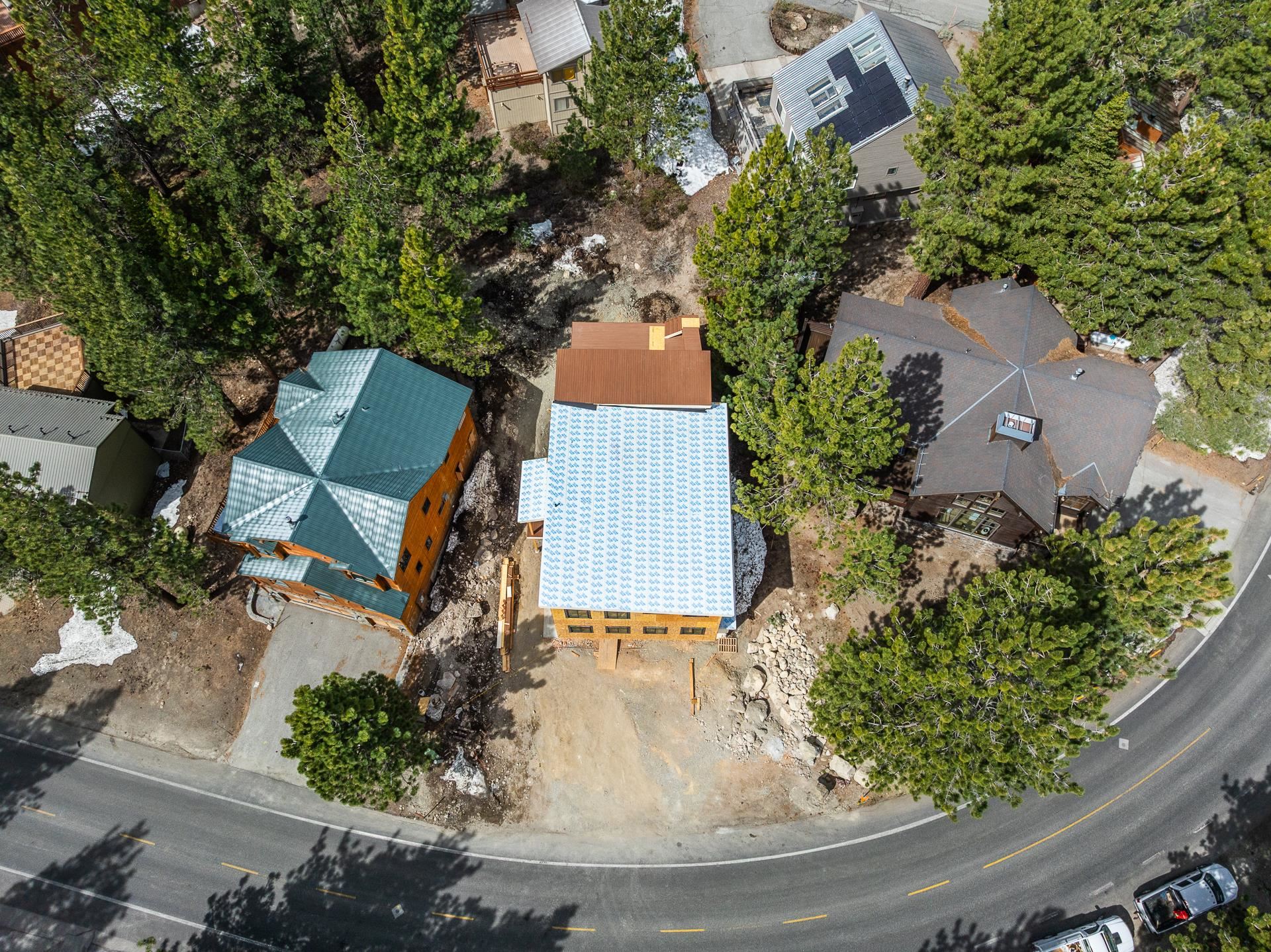 Aerial view of a house under construction among pine trees beside a curved road.