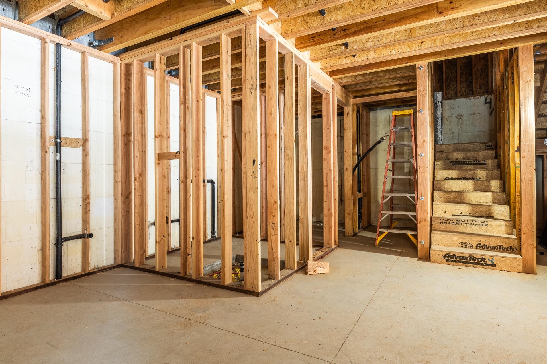 Unfinished interior with exposed wood framing, a concrete slab, and a temporary staircase beside a red ladder.