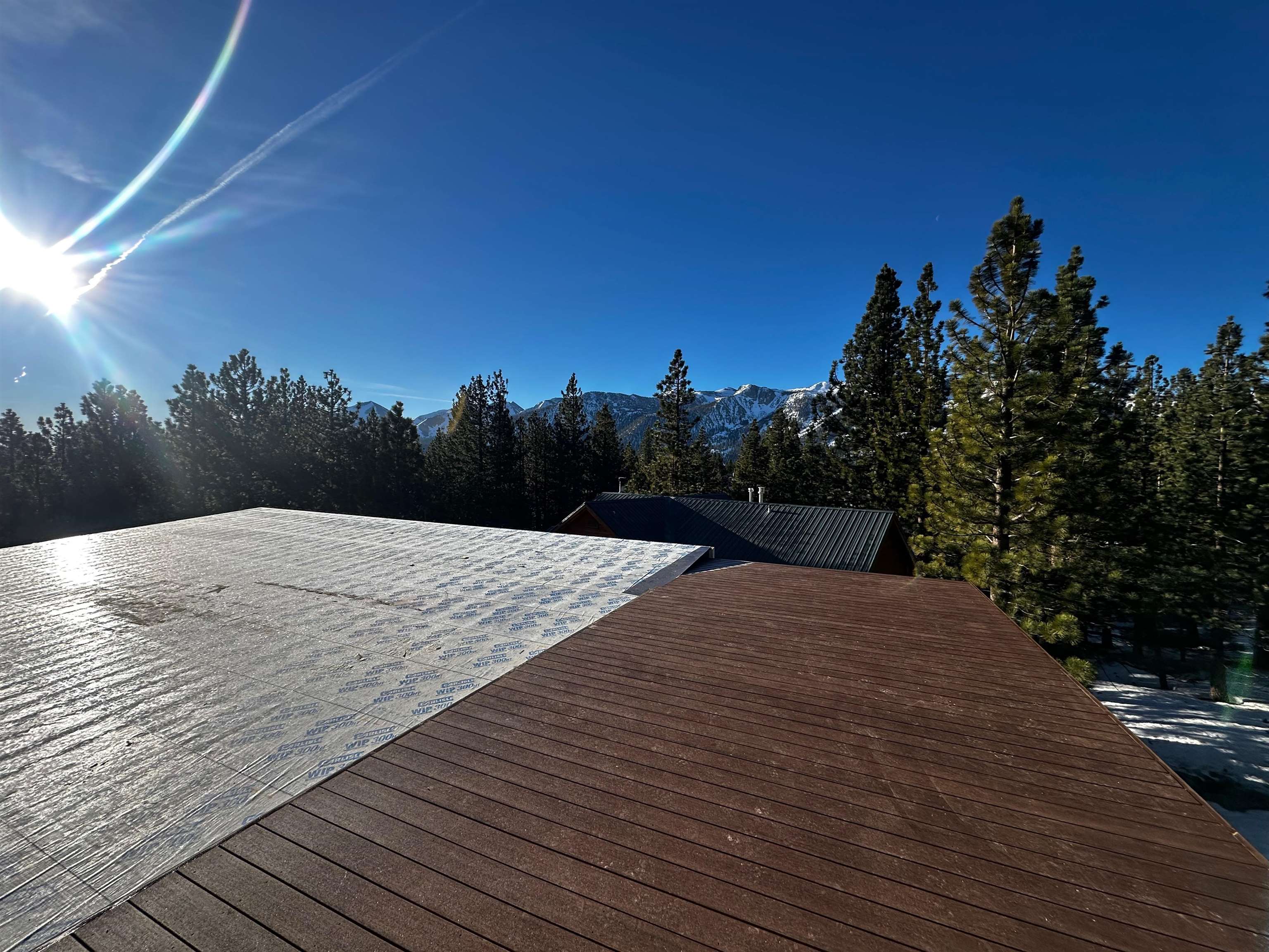 Roof under construction with pine forest and snow-covered mountains beyond.