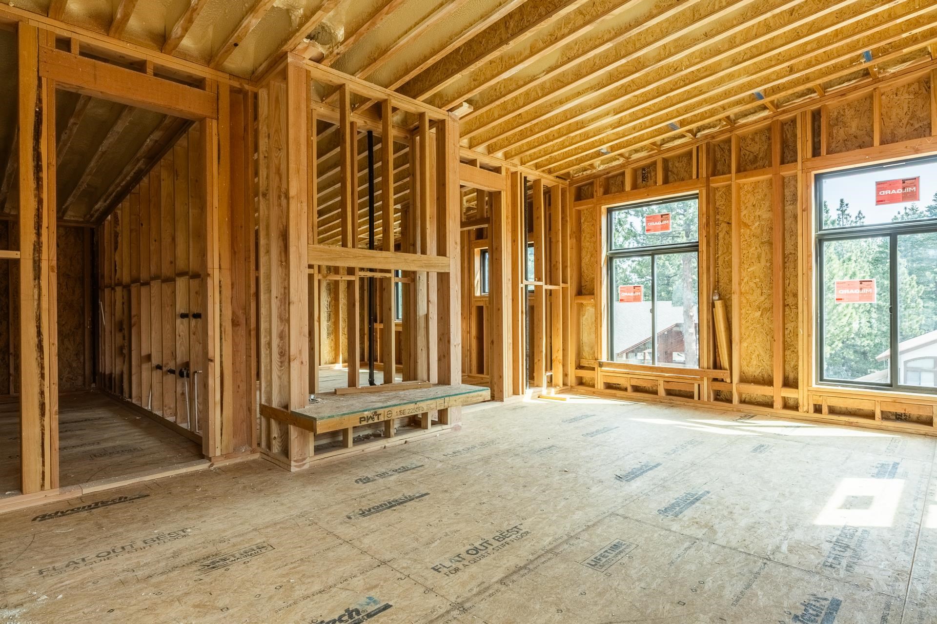 Unfinished room with exposed wood framing, plywood flooring, and large windows.