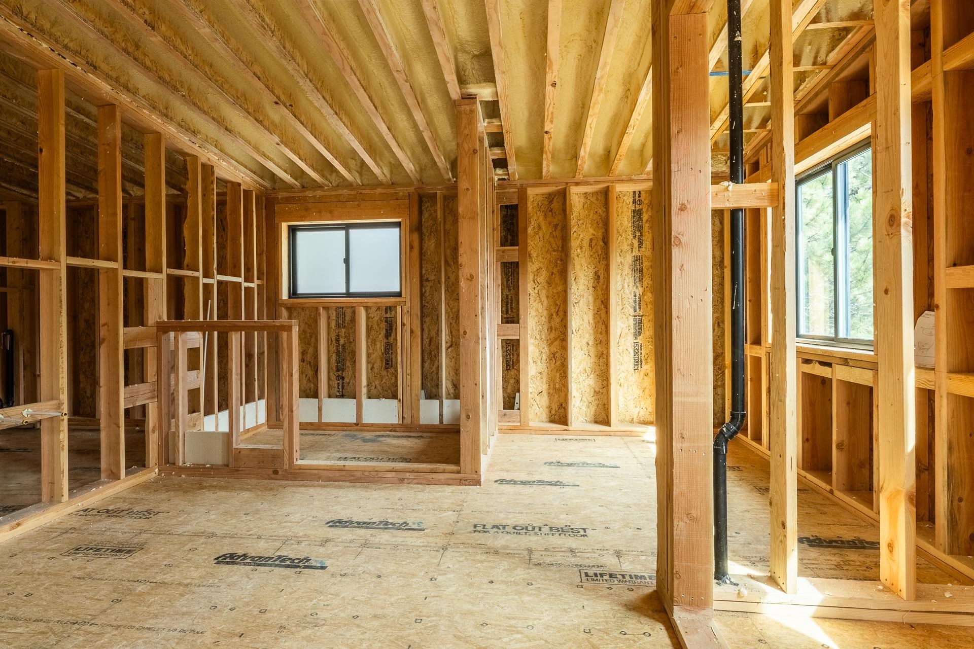 Unfinished room with exposed wood framing, floor sheathing, and sunlight through two windows.