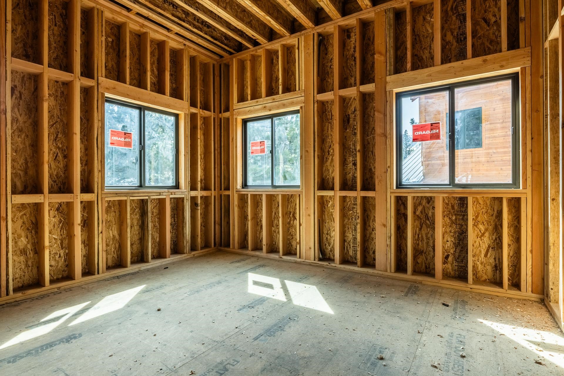 Unfinished framed room with three windows and sunlight on the bare subfloor.