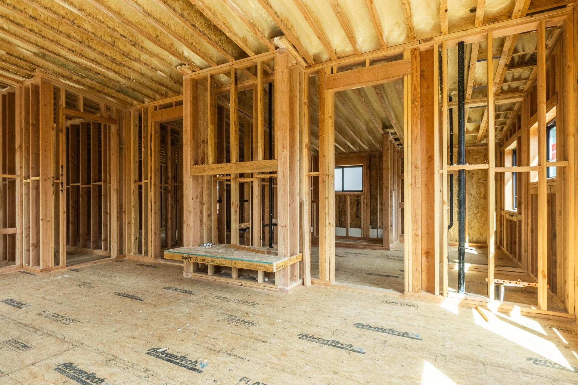 Unfinished house interior with exposed wood framing, ceiling insulation, and plumbing pipes.