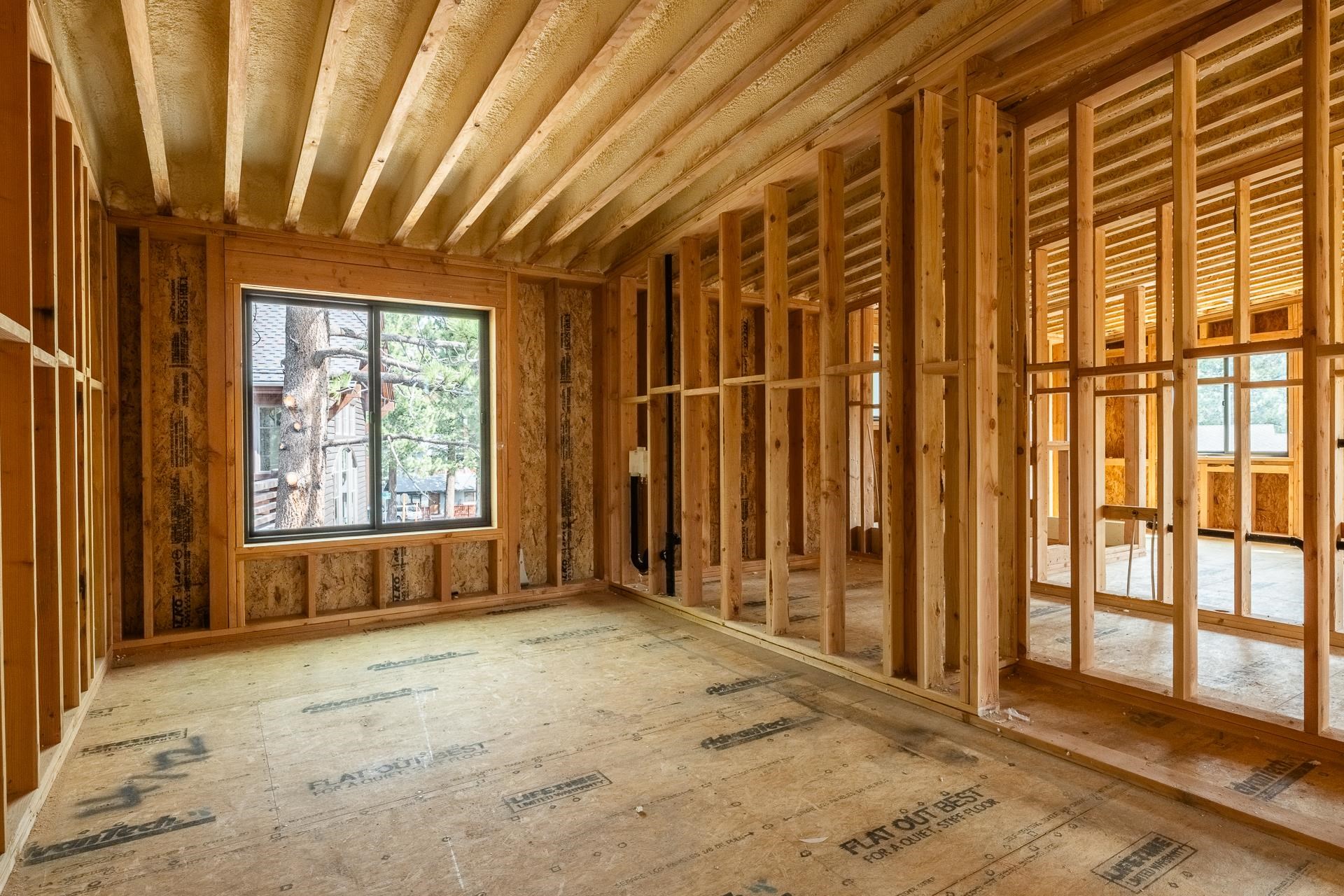 Unfinished framed interior with exposed ceiling joists and a window overlooking trees.