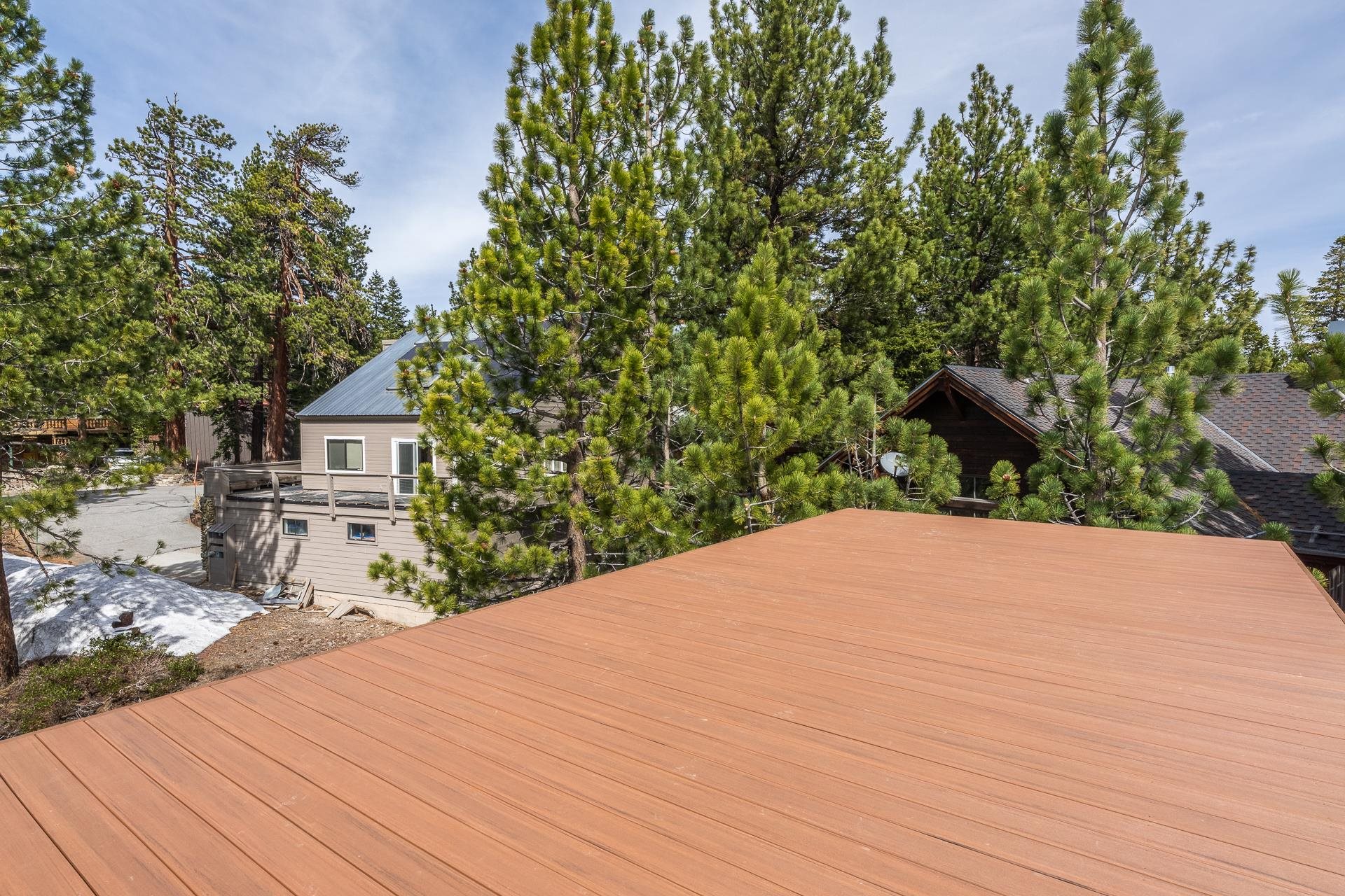 Spacious wood deck overlooking pine trees and nearby homes, with patches of snow below.