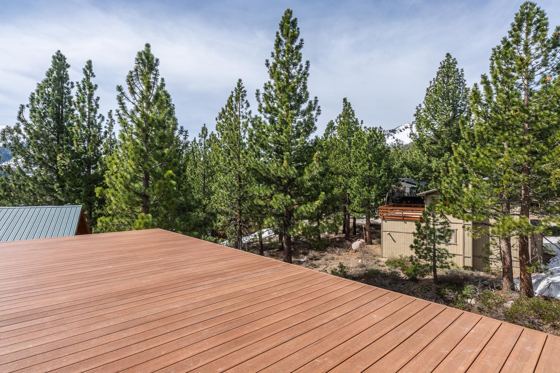 Wide wooden deck overlooking tall pines, neighboring cabins, and a snow-covered mountain peak.