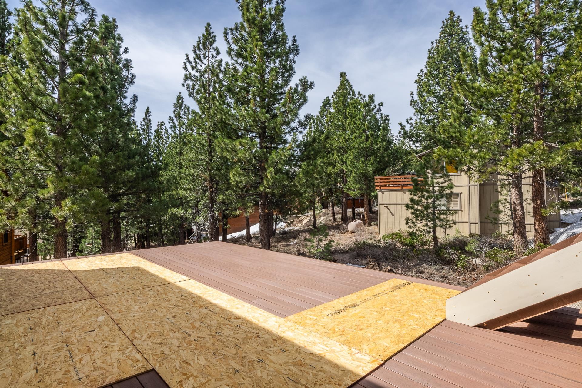 Partially built deck overlooking a pine-covered yard and a home.