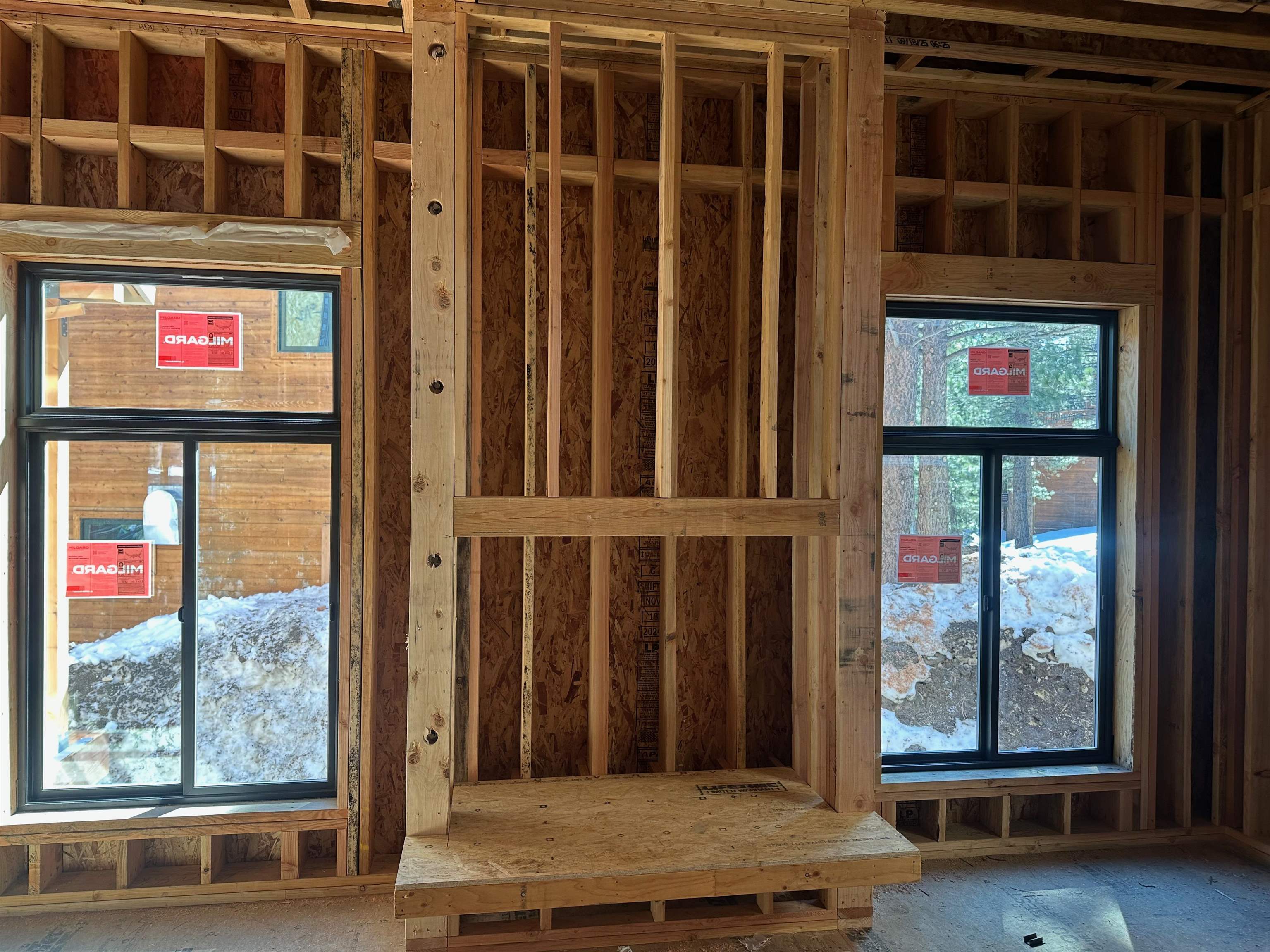 Unfinished interior with exposed wood framing and two black-framed windows overlooking snow.