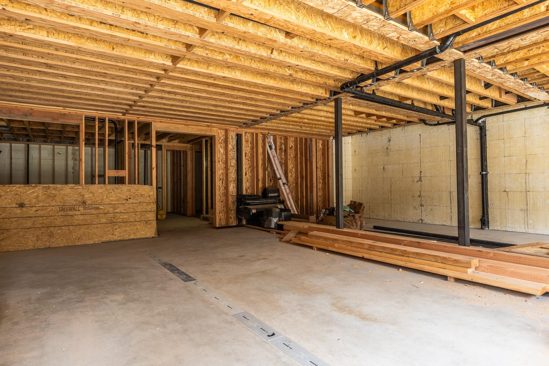 Unfinished basement with exposed framing, concrete floor, support posts, and construction materials.
