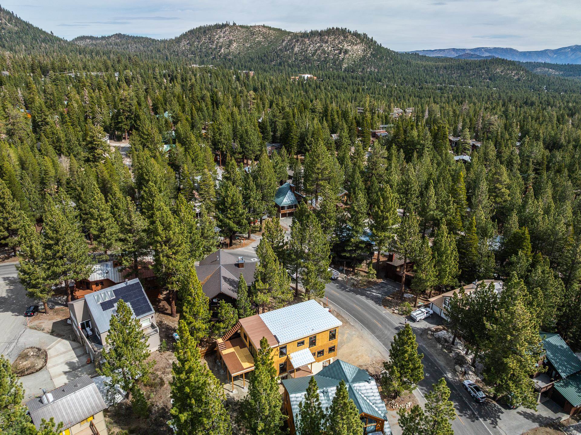 Aerial view of a yellow multi-story home among pine trees, with forested mountains beyond.
