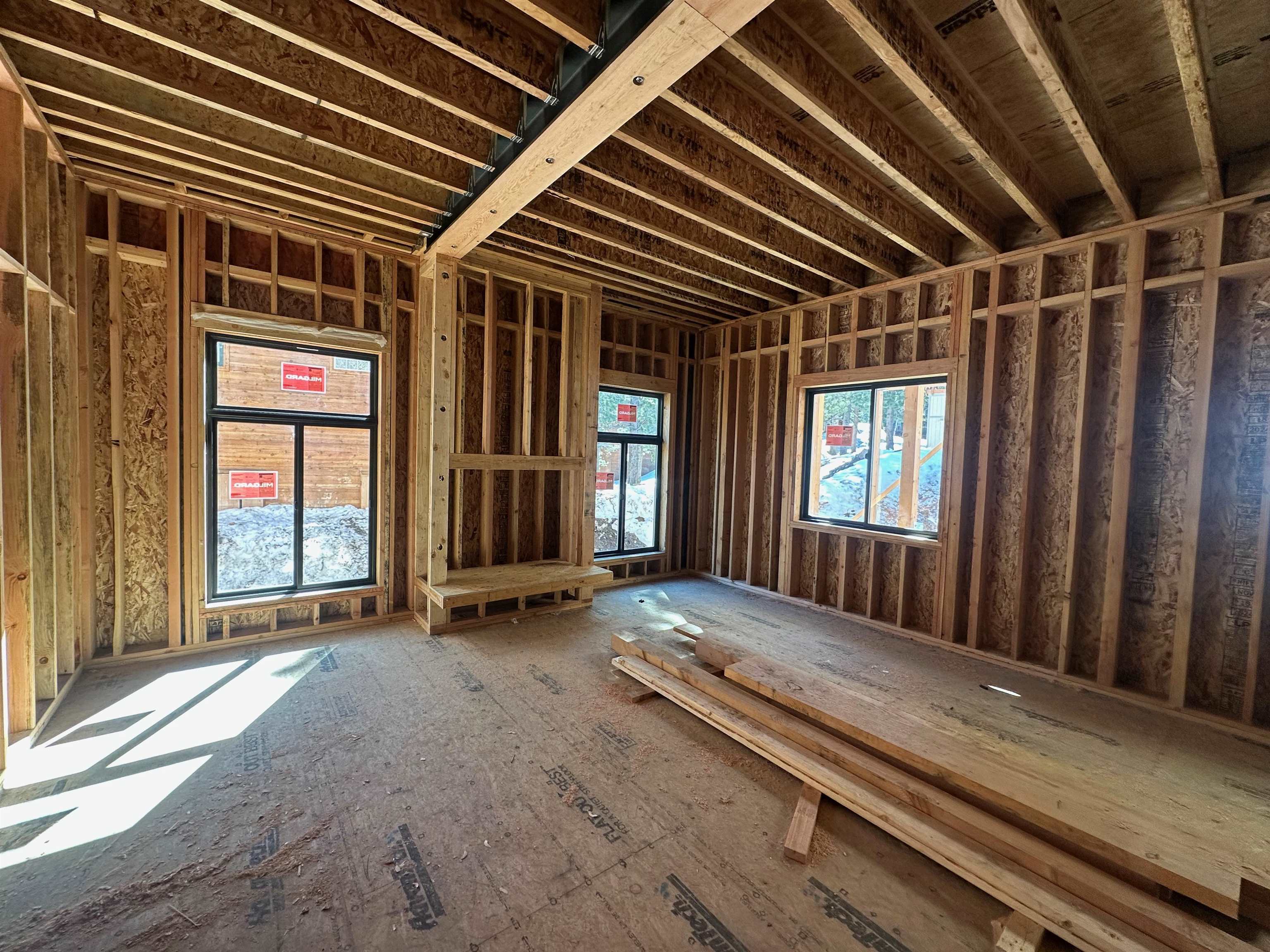 Unfinished room with exposed wood framing, a vaulted ceiling, and windows overlooking snow.