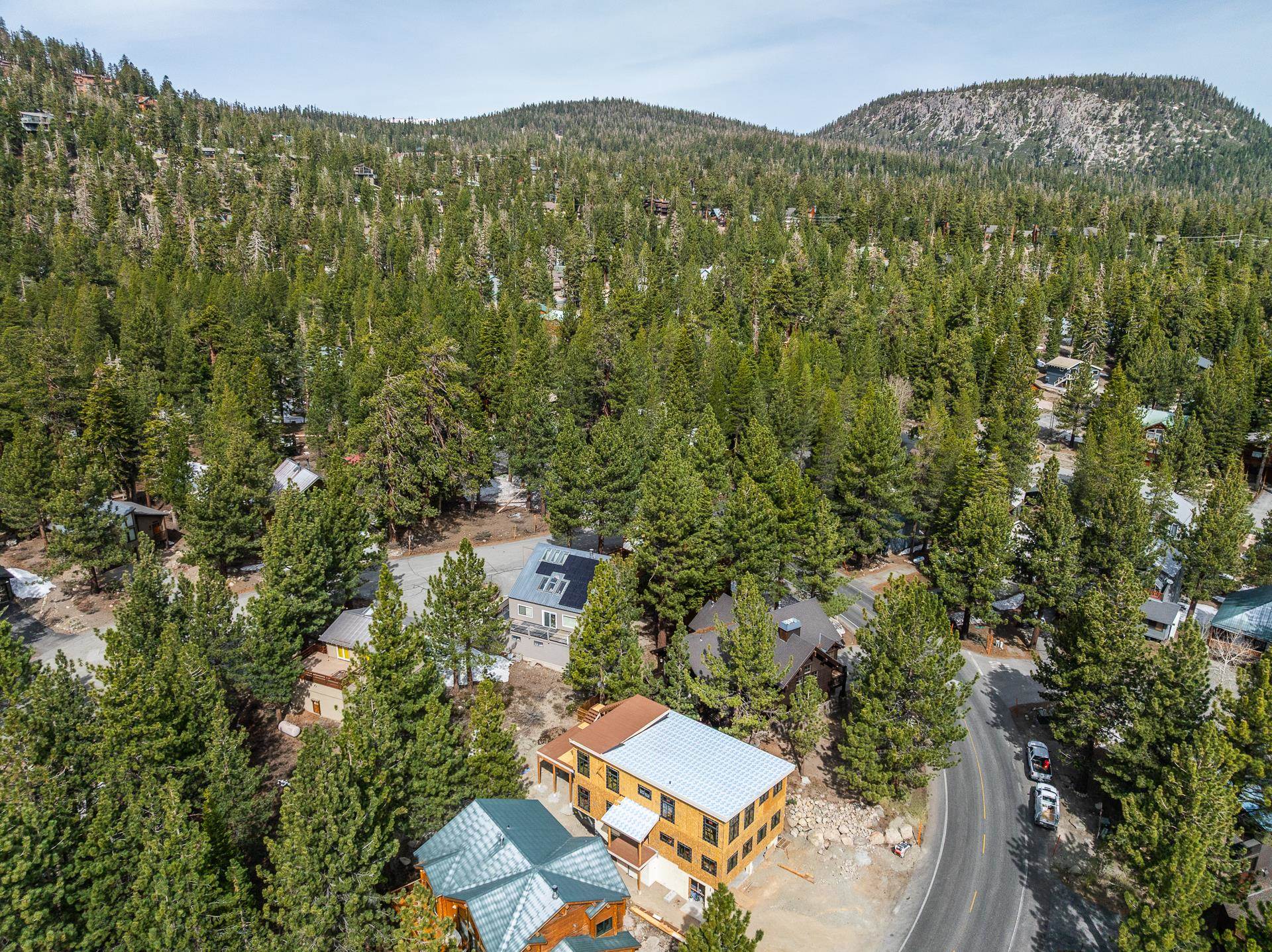 Aerial view of a mountain neighborhood, with a large orange-brown house beside a winding road.