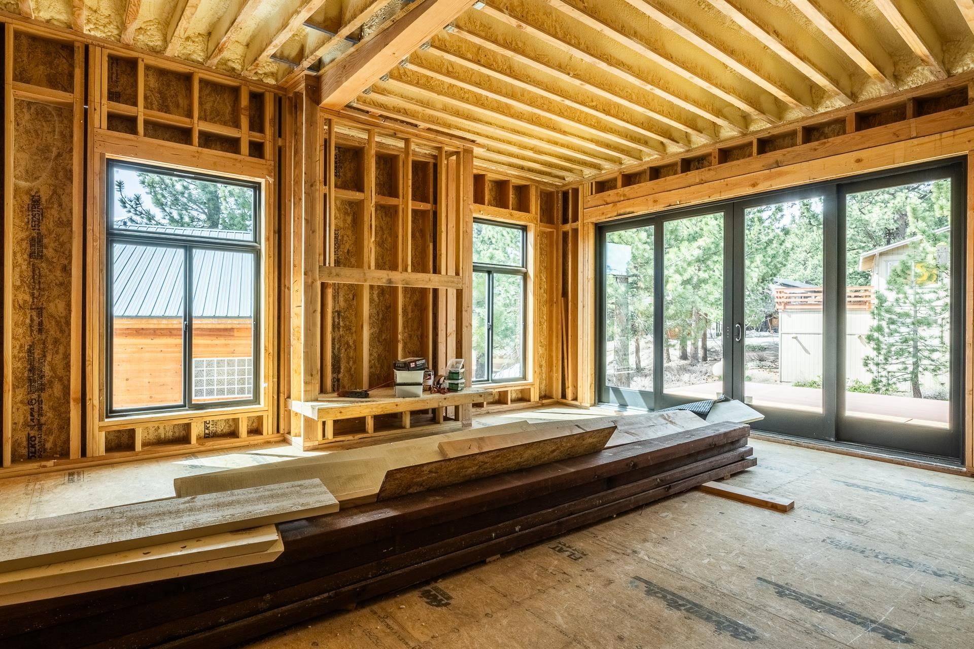 Unfinished room with exposed framing, insulated ceiling, large windows, and lumber stacked on the floor.