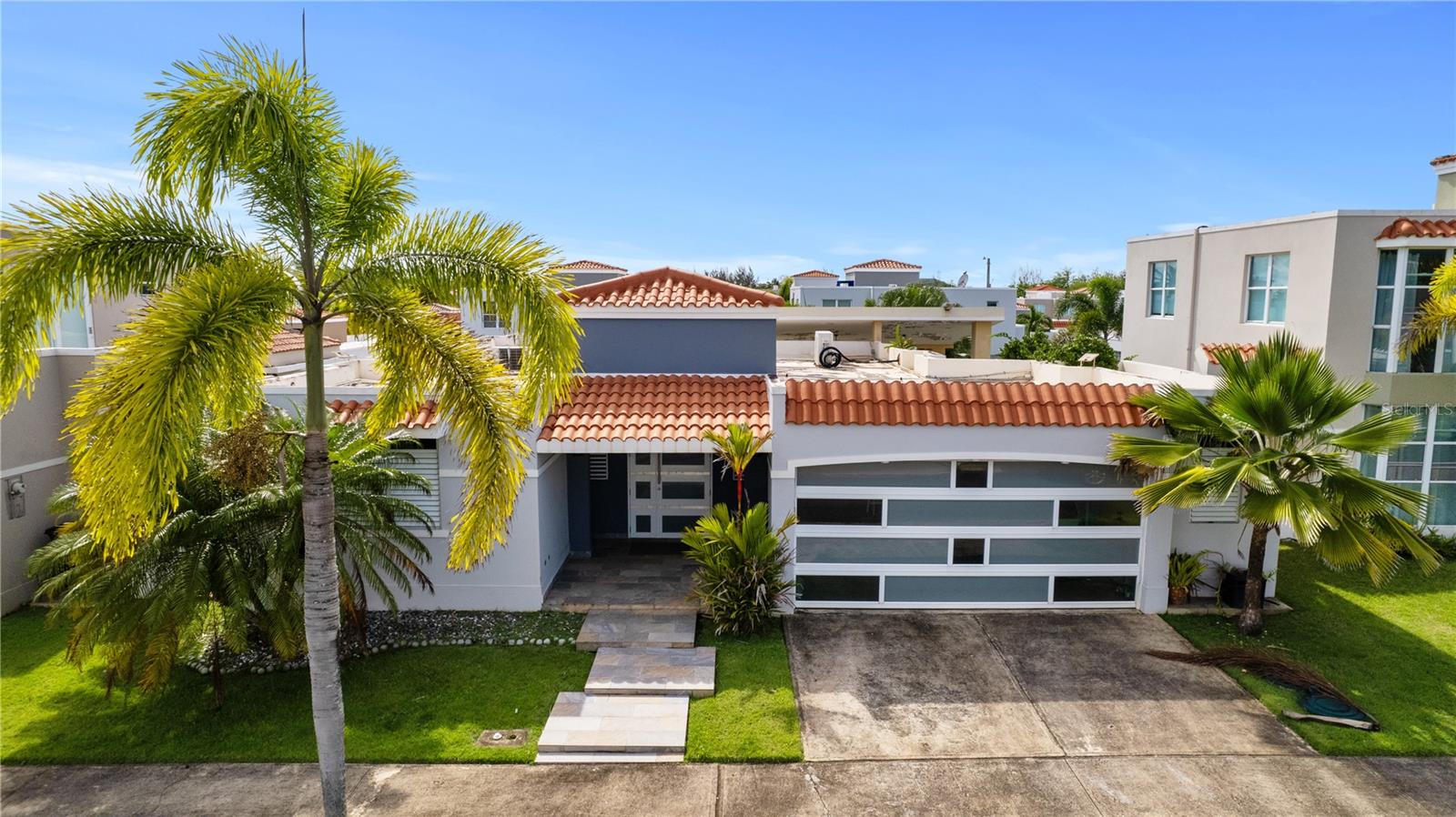 Modern home with terracotta tile roofs, broad windows, palm trees, and a front driveway.