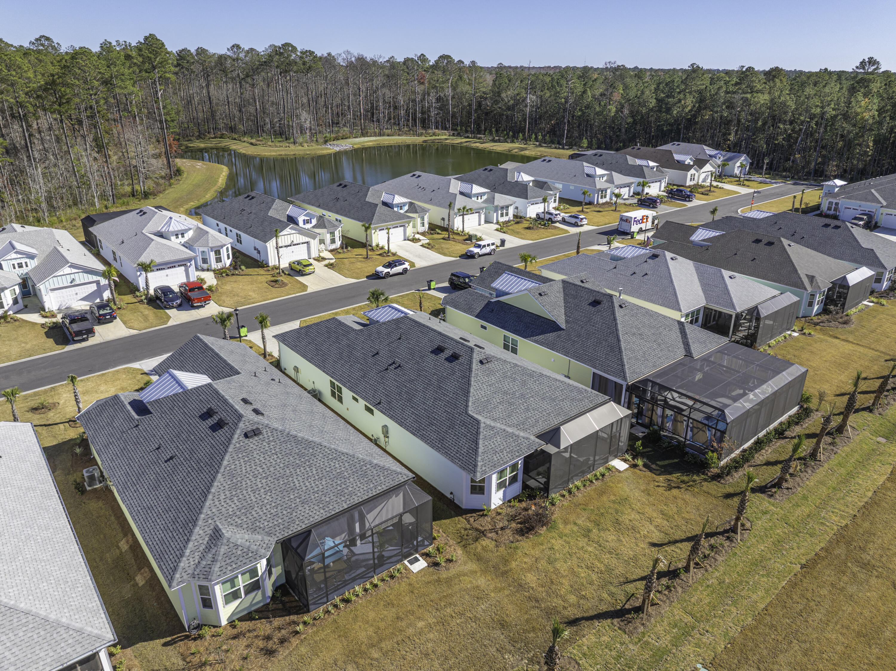 Aerial neighborhood view with detached homes, screened lanais, and a tree-lined pond.