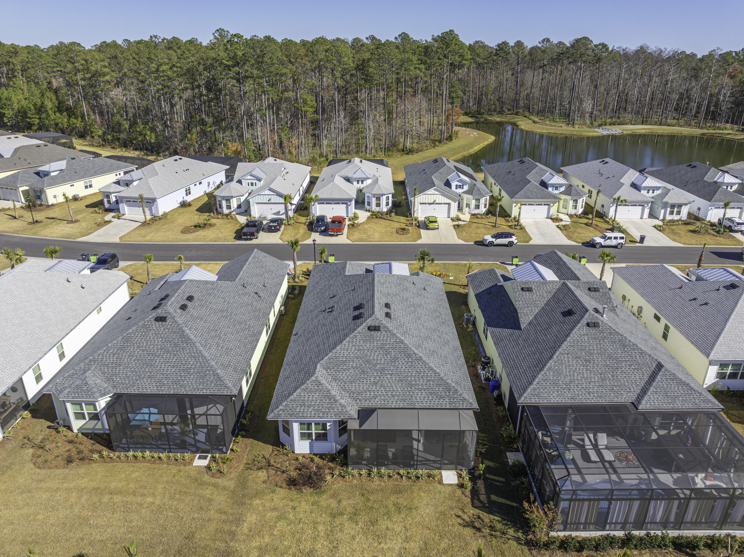 Aerial view of homes with screened patios beside a wooded pond.