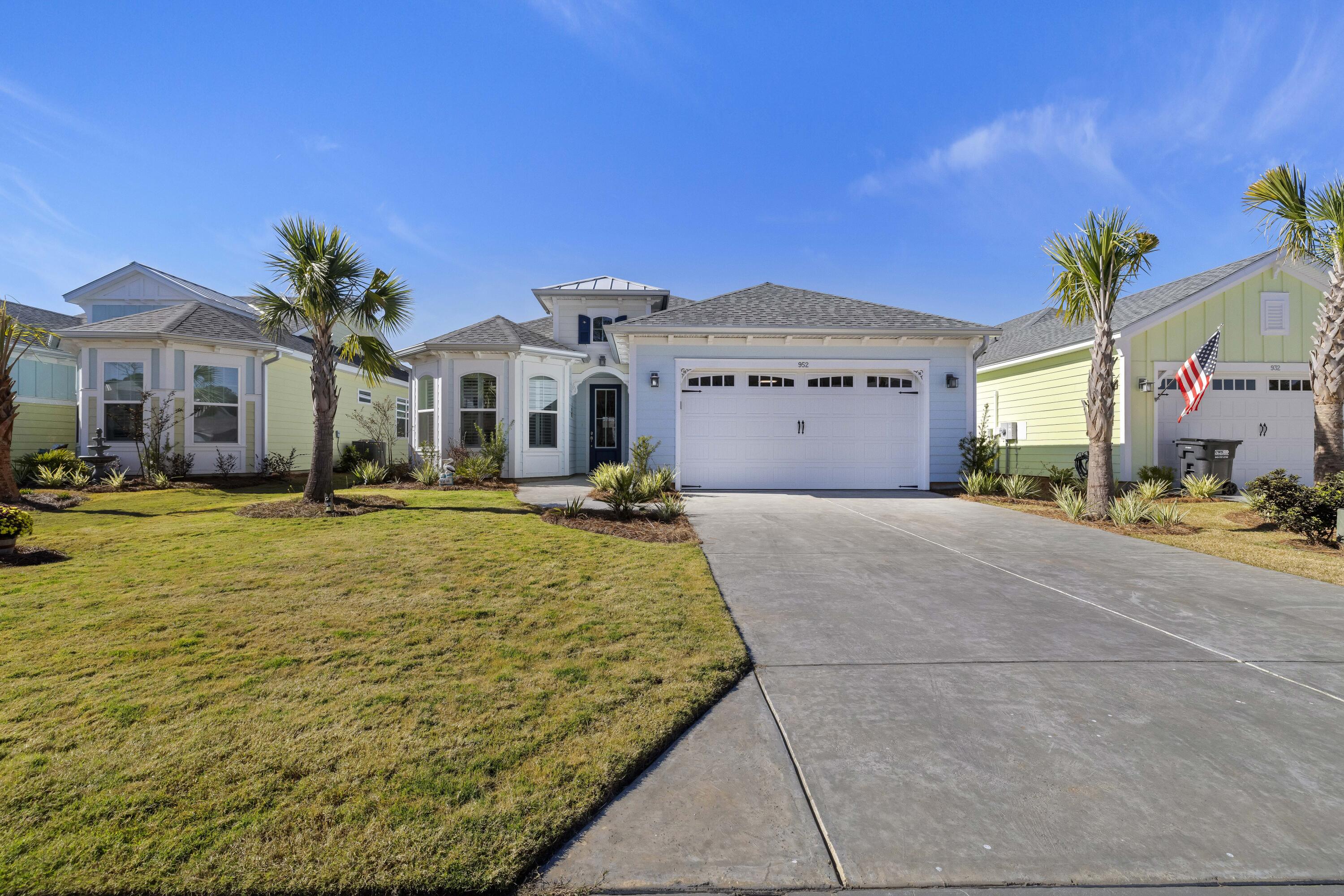 Light blue house with a white double garage, palm trees, and a broad concrete driveway.