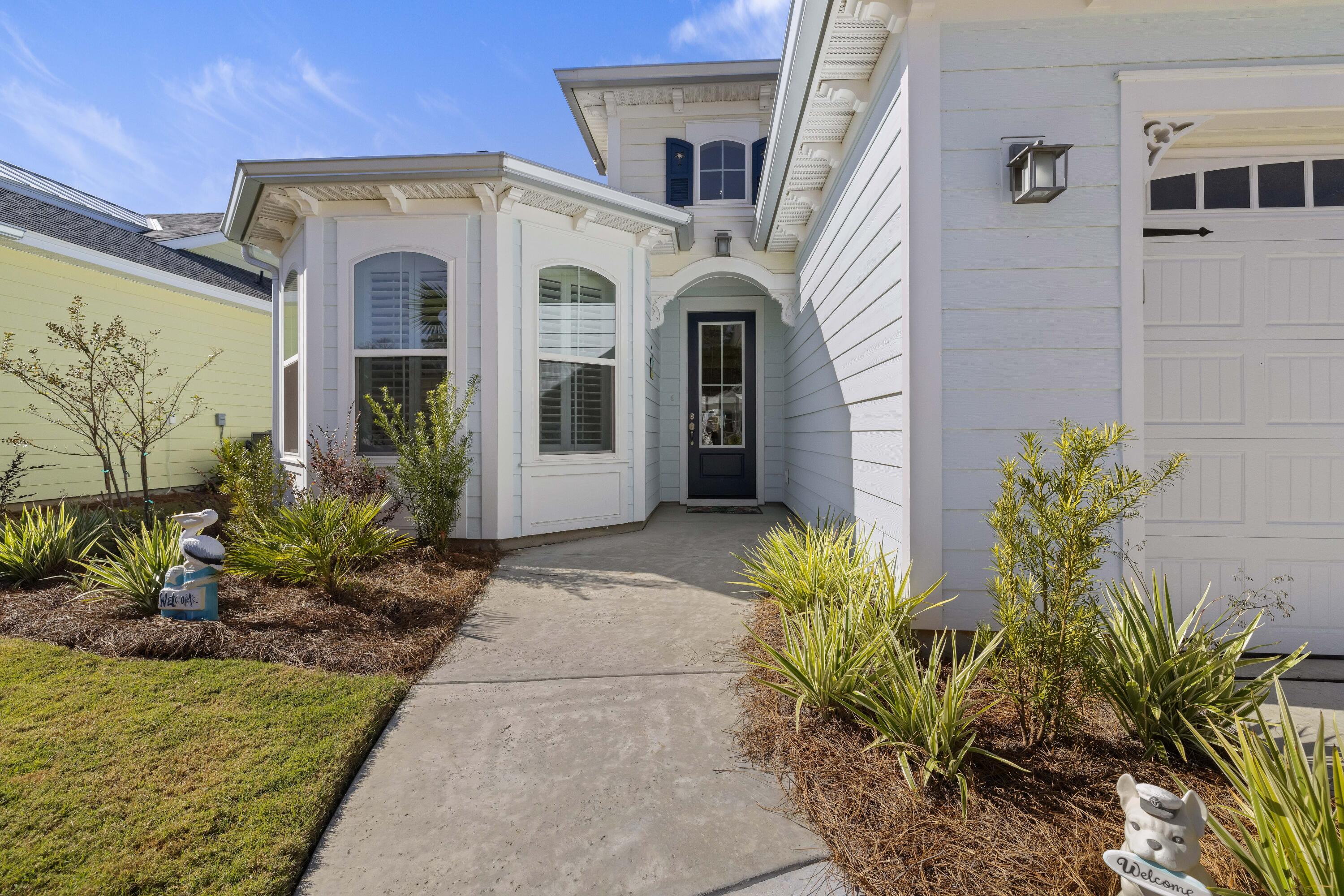 House entrance with a recessed dark door, shuttered bay windows, landscaped walkway, and attached garage.