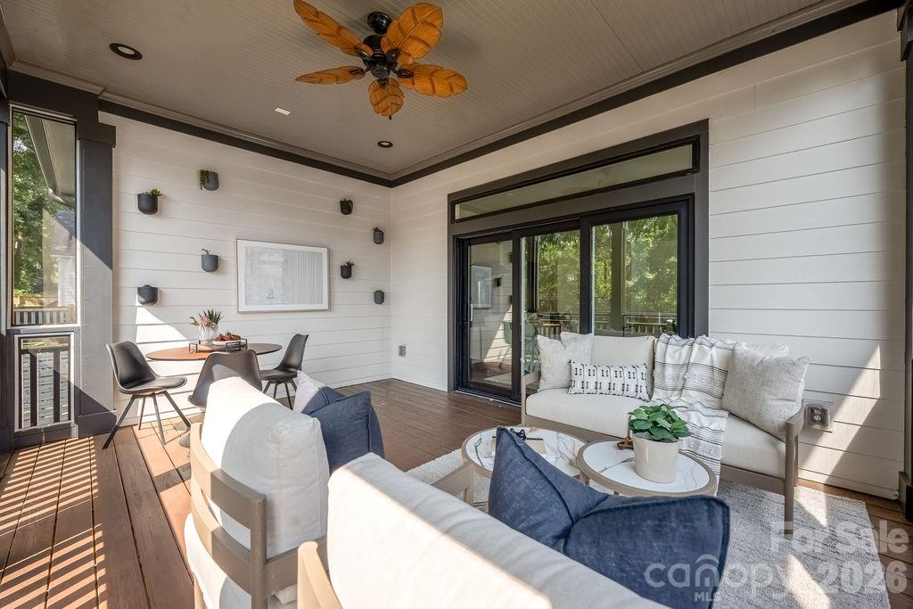 Covered porch with a wood-plank floor, white seating, dining table, and ceiling fan.