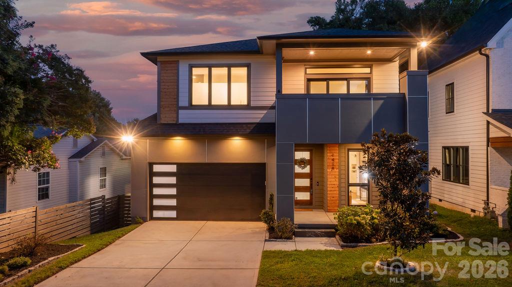 Modern two-story home with a dark garage door and illuminated entry at dusk.