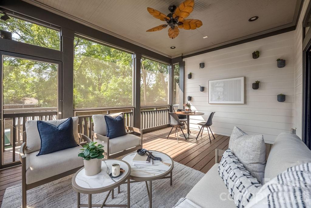 Furnished sunroom with large windows, white seating, a wood floor, and a ceiling fan.