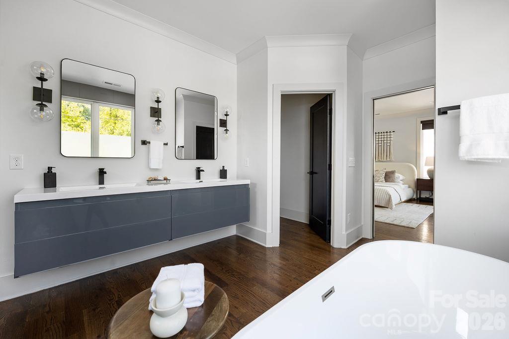 Contemporary bathroom with a gray double vanity, dark wood floors, and a large white soaking tub.