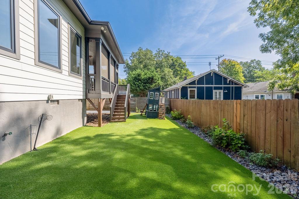 Side yard with green lawn, raised deck and stairs, and a wooden privacy fence.