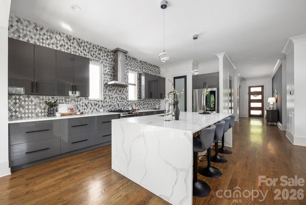Modern kitchen with a large marble island, dark cabinetry, and patterned tile backsplash.
