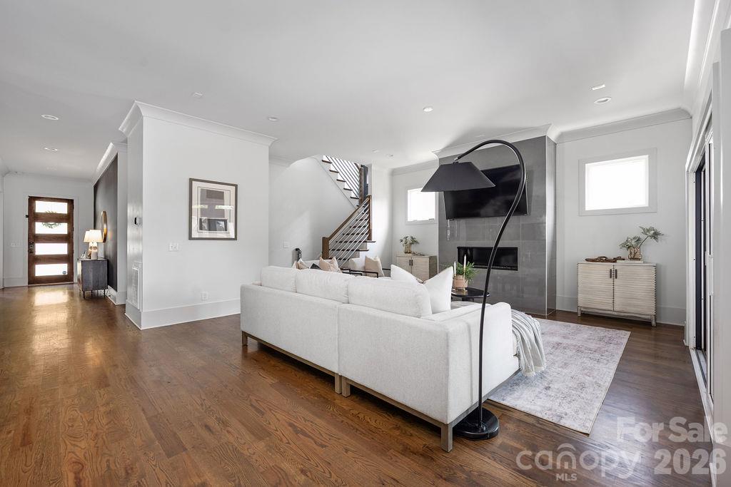 Furnished living room with white sofas, hardwood floors, tiled fireplace wall, and an open staircase.