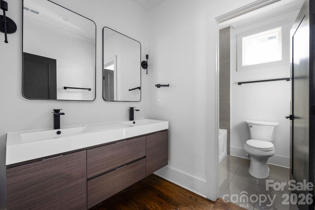Modern bathroom with a double-sink wood vanity, black fixtures, and a separate toilet area.