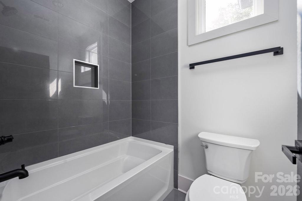 Bathroom with a white tub, dark tiled shower wall, recessed niche, and high window.