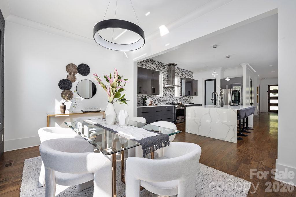 Staged dining area opens to a modern kitchen with a marble island and dark cabinetry.