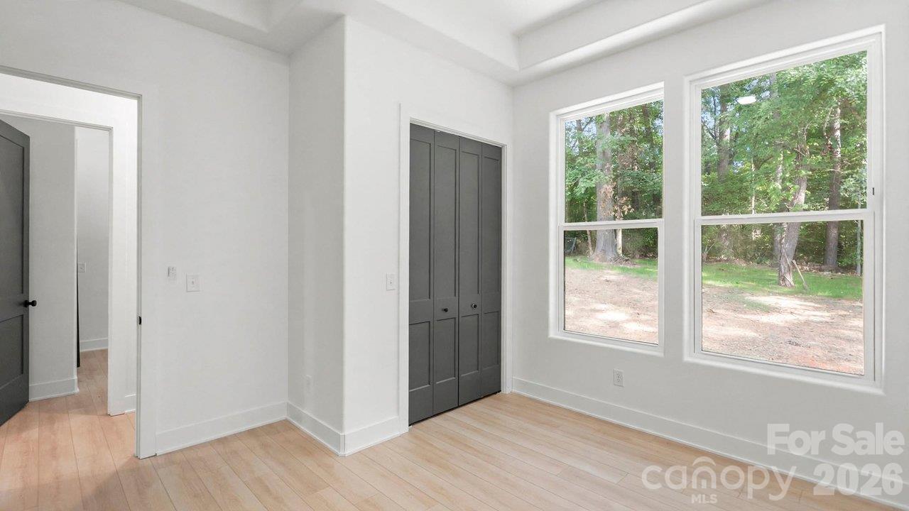 Bright bedroom with gray closet doors, pale wood flooring, and large windows overlooking trees.