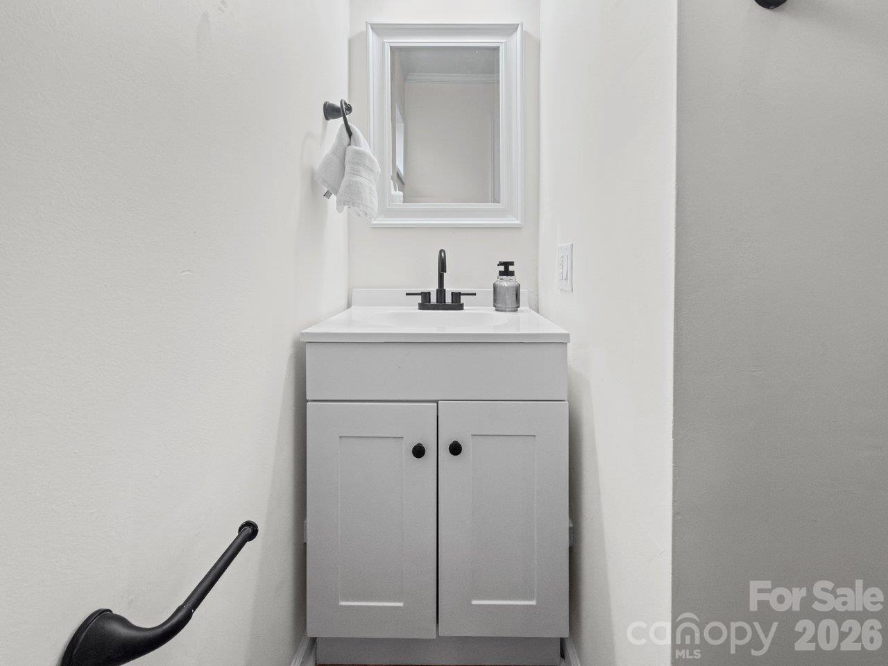 White bathroom vanity with black faucet, framed mirror, and hand towel.