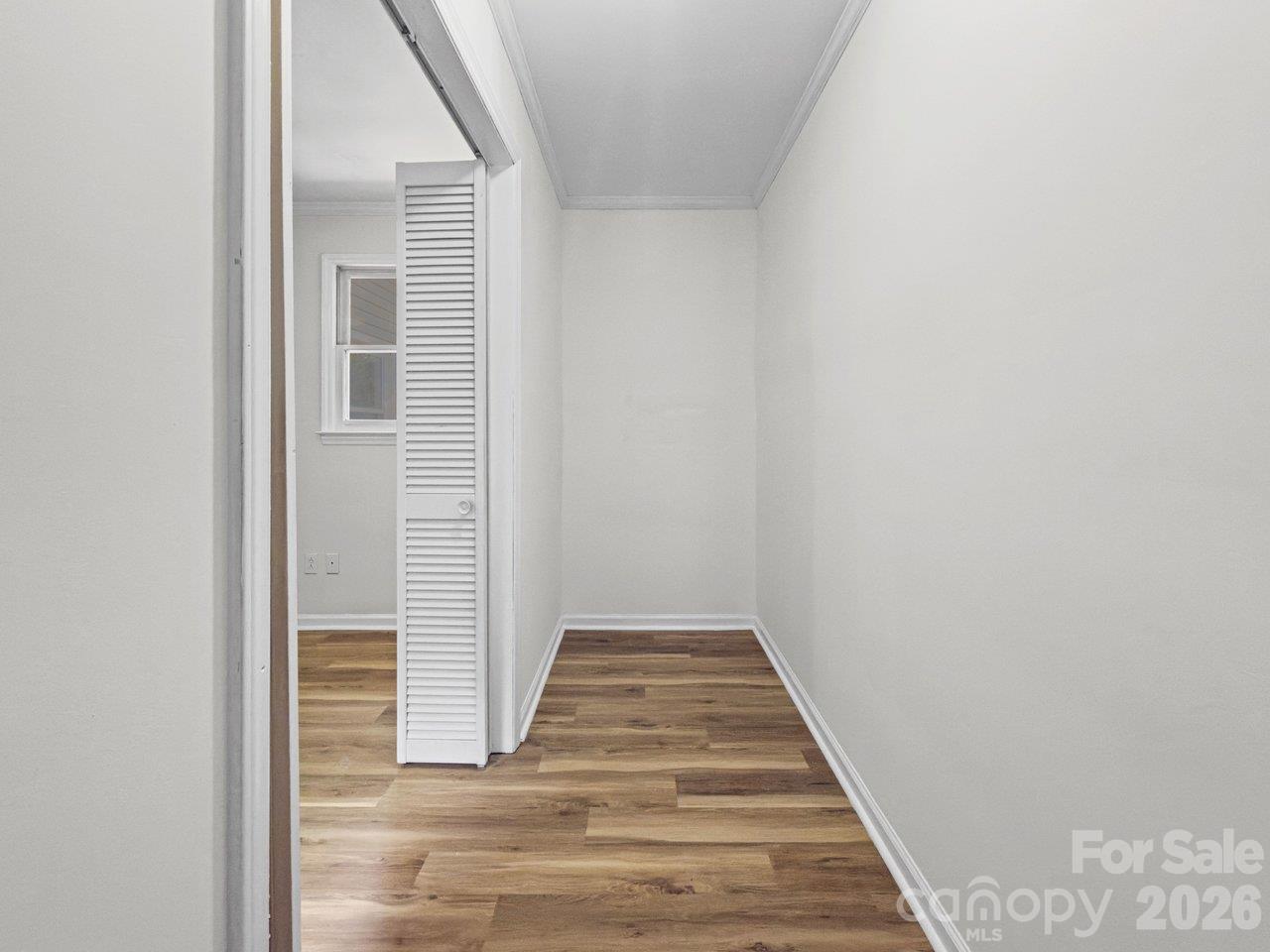 Narrow empty room with wood-look flooring and an open louvered door.
