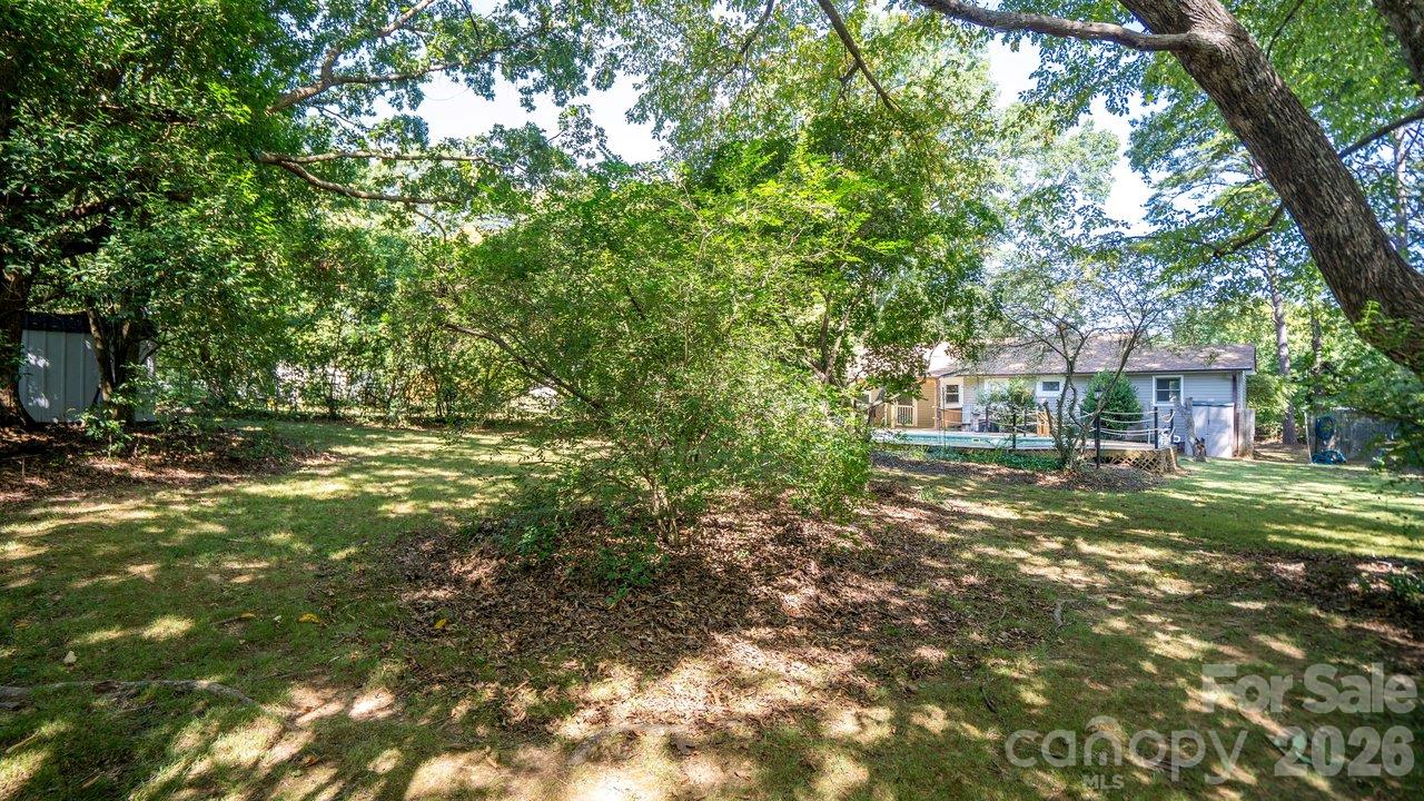 Tree-shaded backyard with a lawn, above-ground pool, and rear view of the house.
