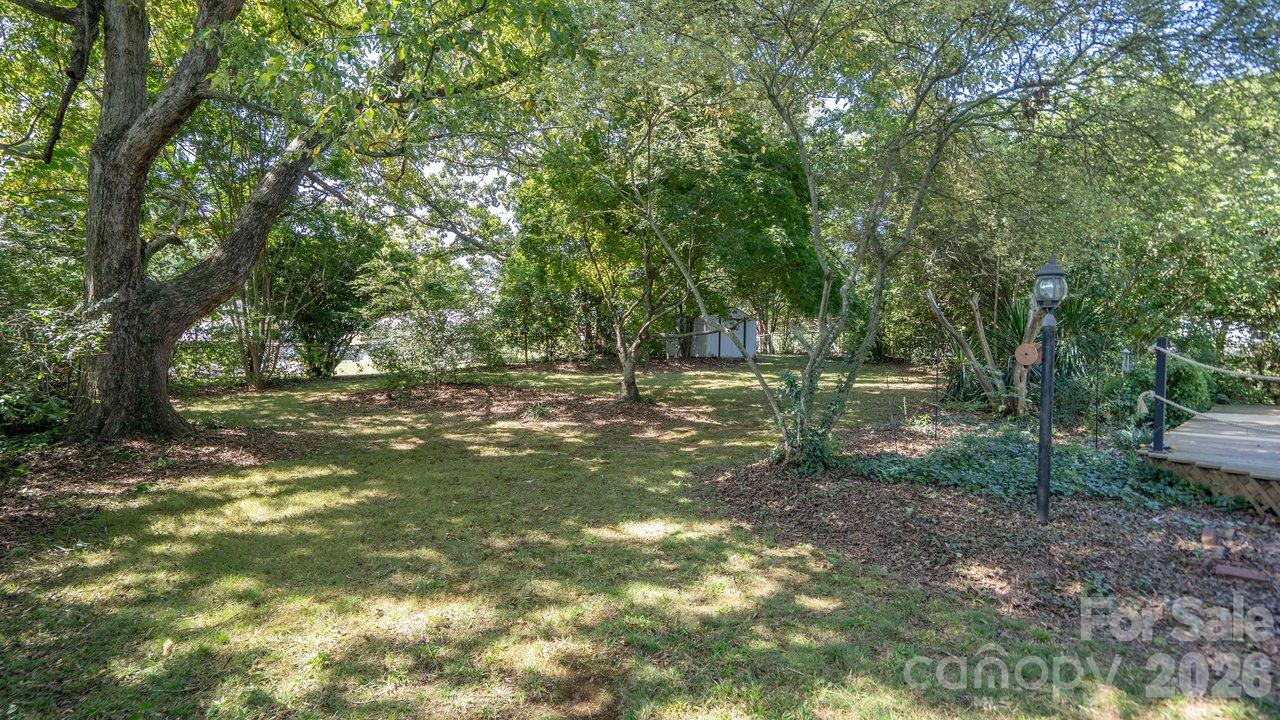 Shaded backyard with a broad lawn, mature trees, and a raised deck along the right edge.