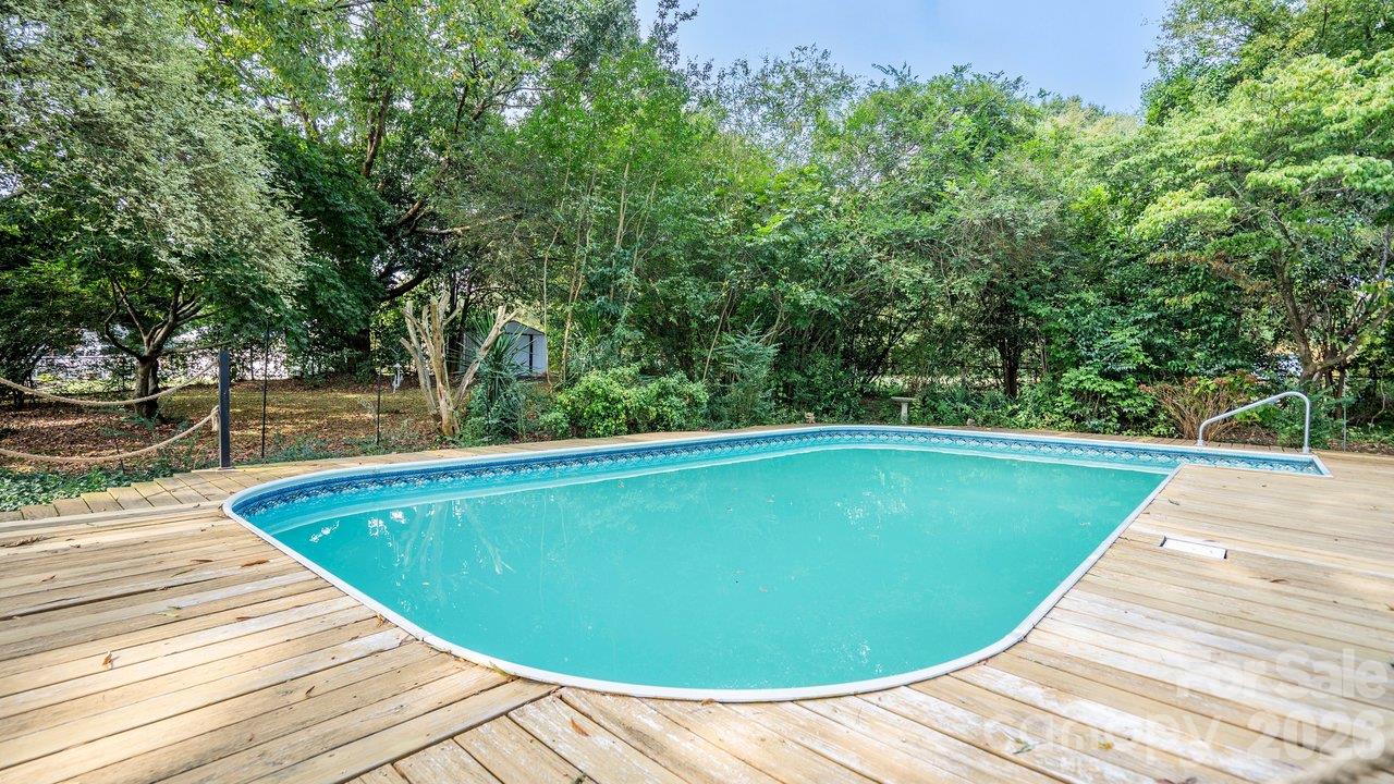 Backyard swimming pool on a wooden deck, surrounded by mature trees and greenery.