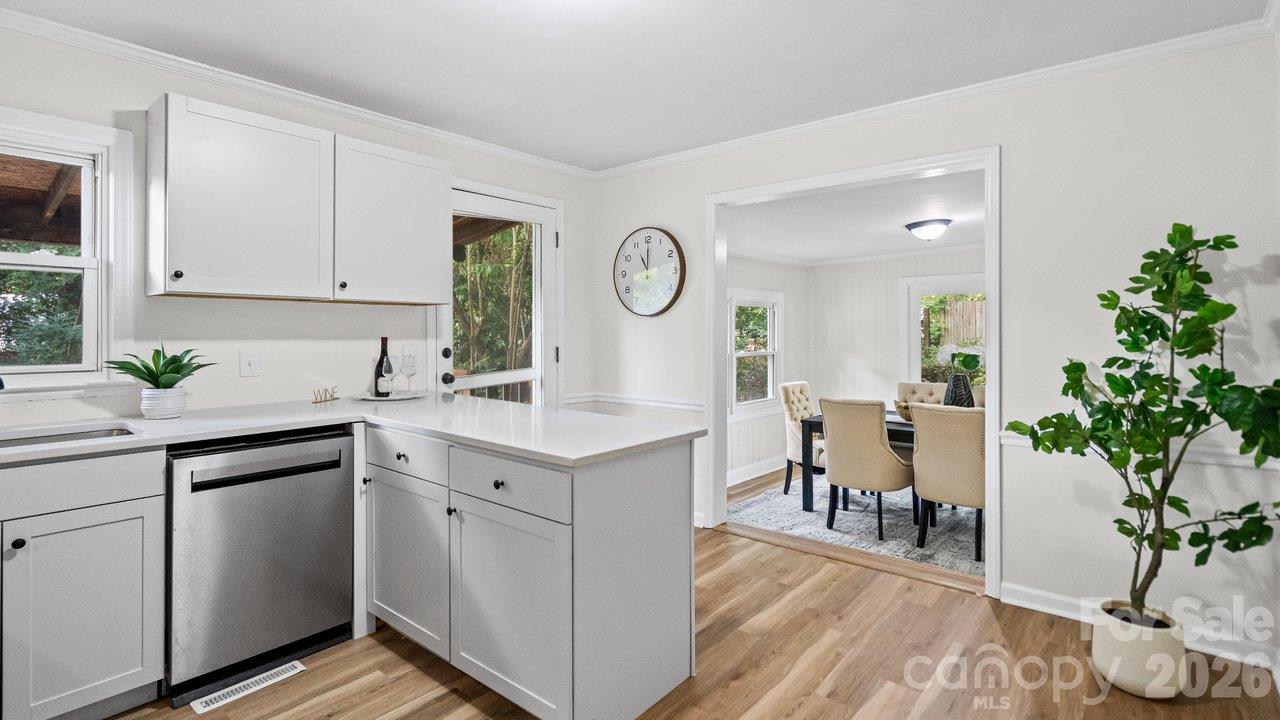 White kitchen with peninsula and stainless-steel dishwasher opening into a furnished dining room.