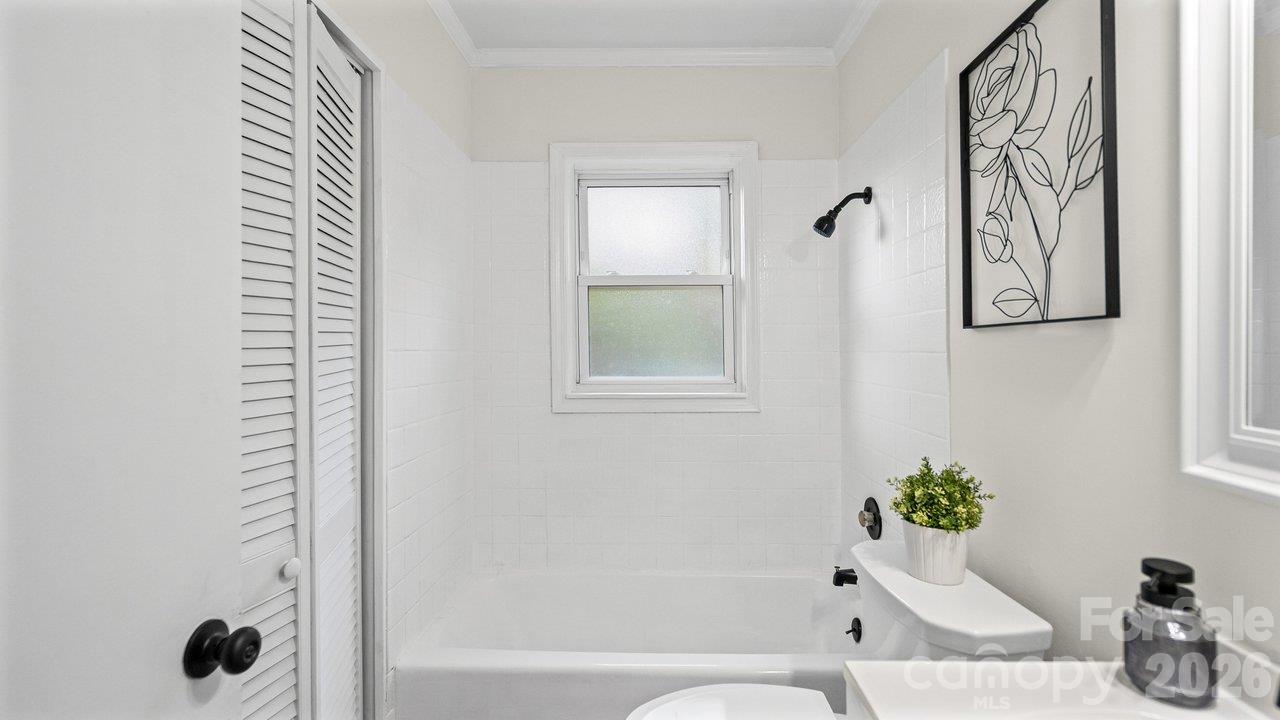 White bathroom with a bathtub, tiled shower, frosted window, and black fixtures.