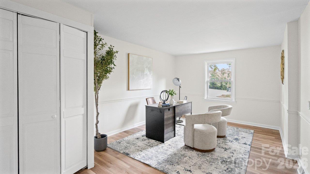 Staged home office with a dark desk, cream chairs, patterned rug, and white paneled closet doors.